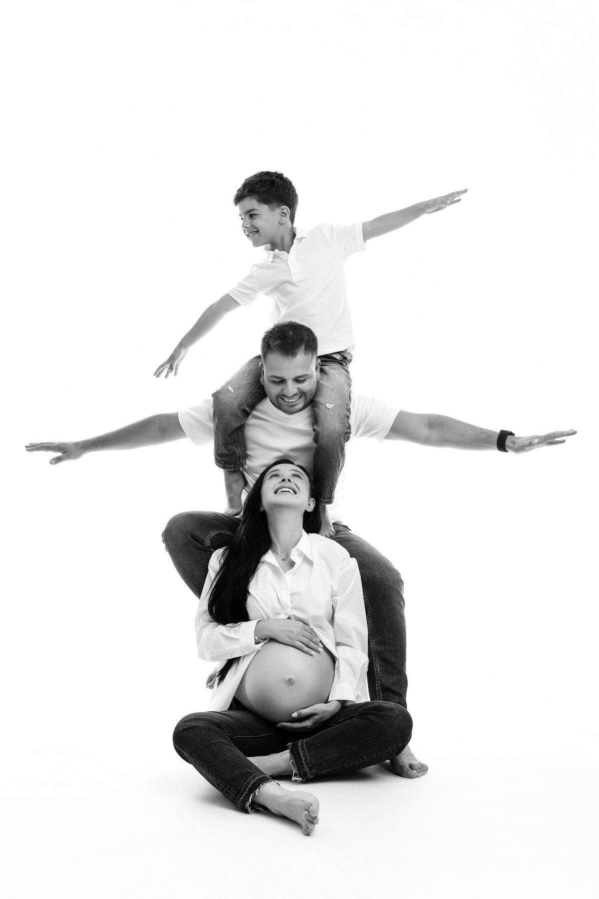 Black and white family and maternity photograph — father with son on his shoulders and expecting mother