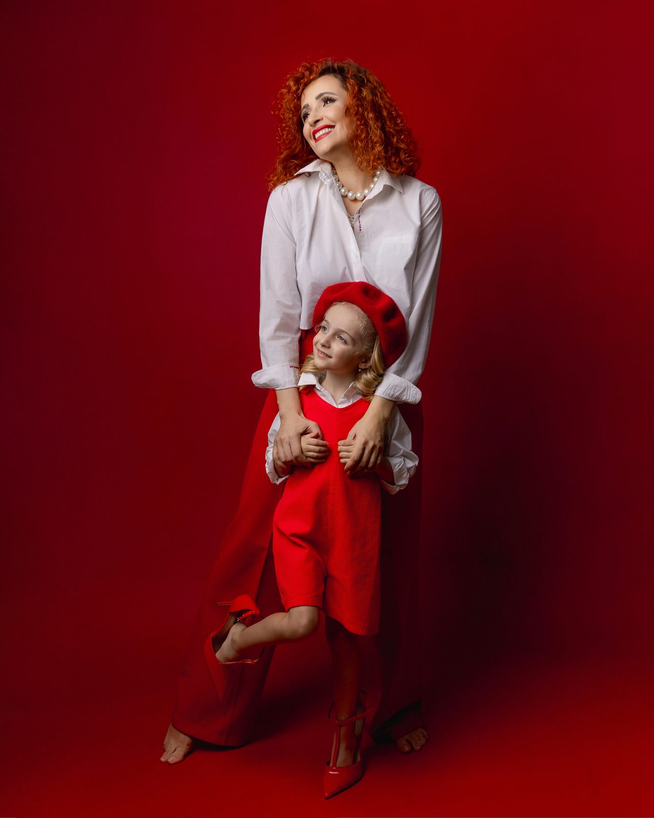 Mother and daughter in red outfits, studio photo session on a red backdrop